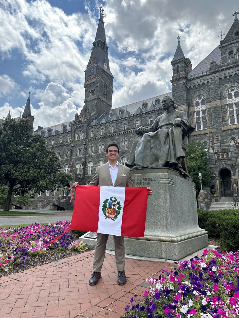 Young man in suit in front of Healy Hall holding a Peruvian flag