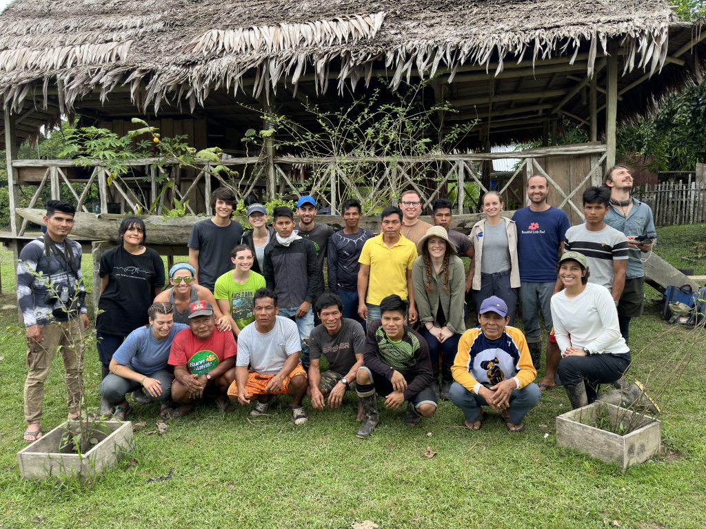A group photo of 15+ people in front of a hut
