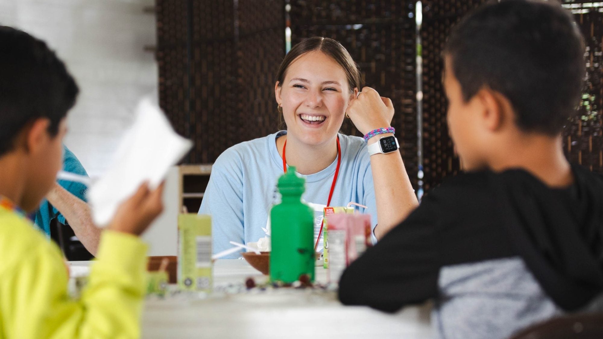 A young woman smiles while sitting with two boys at a table.