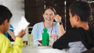 A young woman smiles while sitting with two boys at a table.