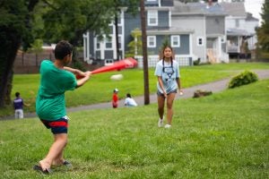 A boy hits a ball with a baseball bat on a grass field.