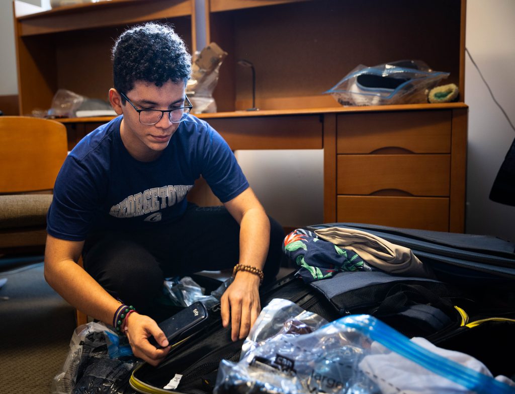 A male college student unpacks his belongings from his suitcase in his dorm room.