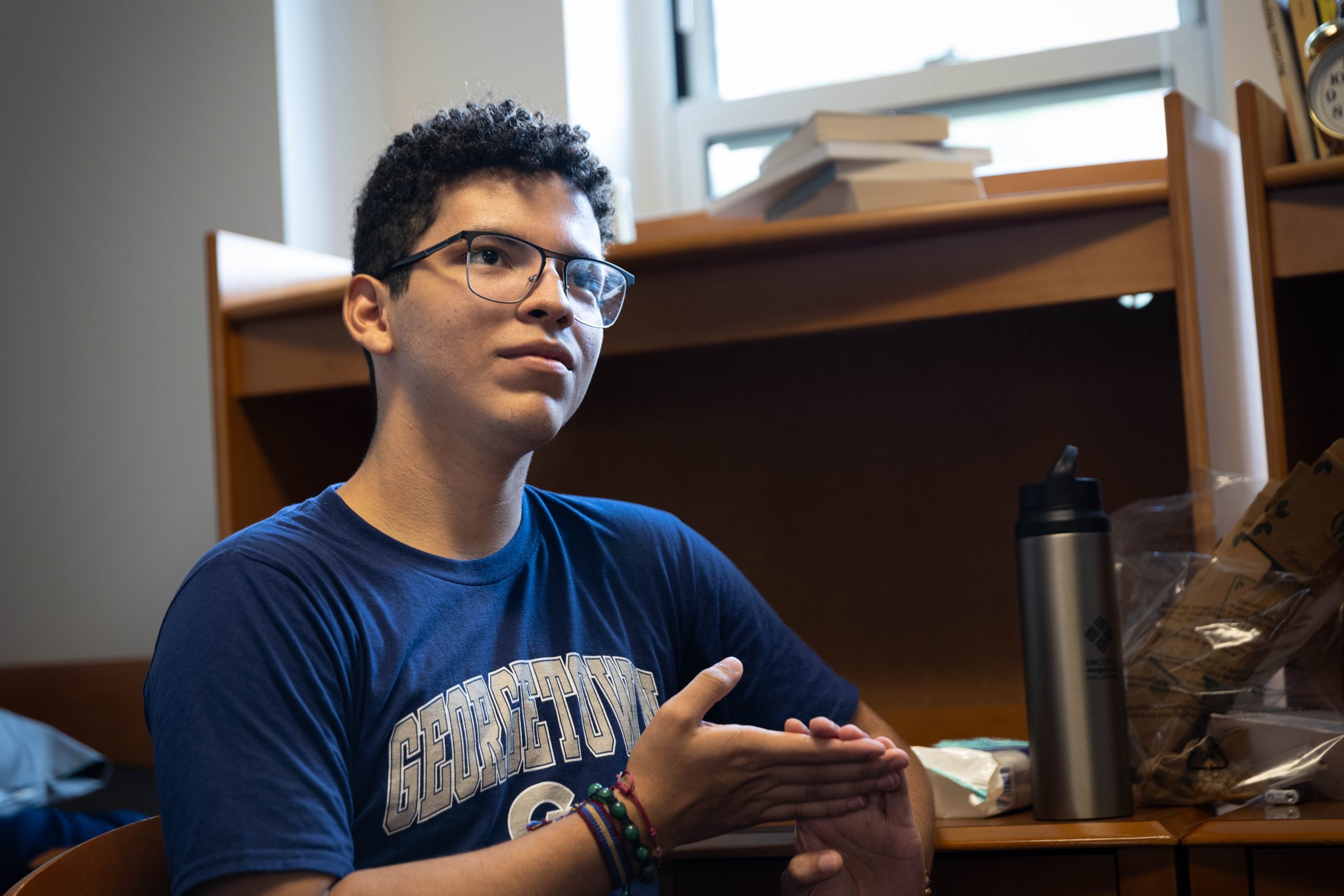 A male college student looks reflectively off-camera. He wears glasses and a blue Georgetown T-shirt.