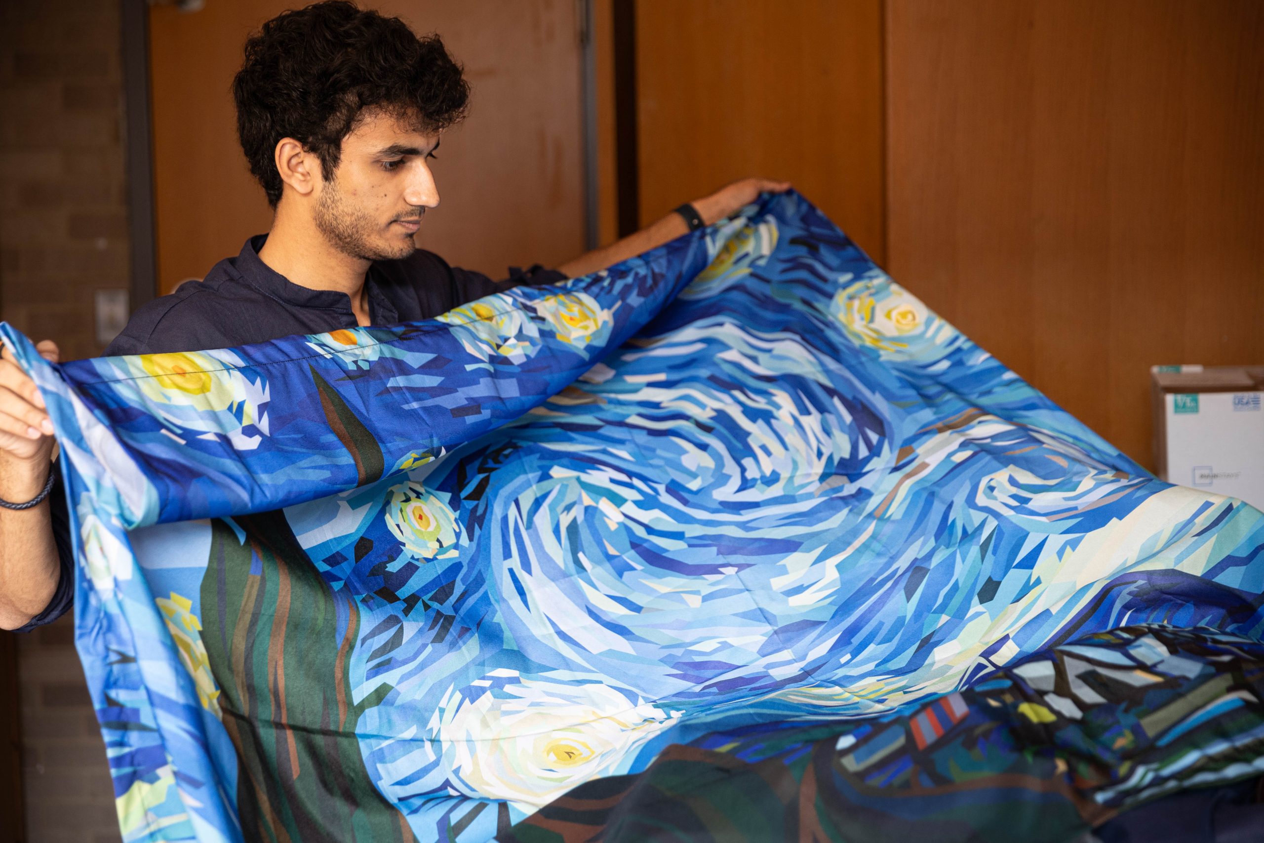 A male college student holds up a large tapestry of Vincent van Gogh's painting, "The Starry Night."