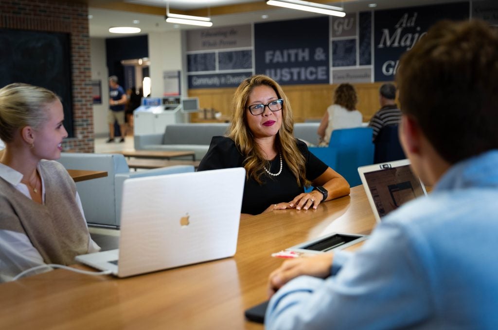 Woman sitting at a table with several students with laptops open.