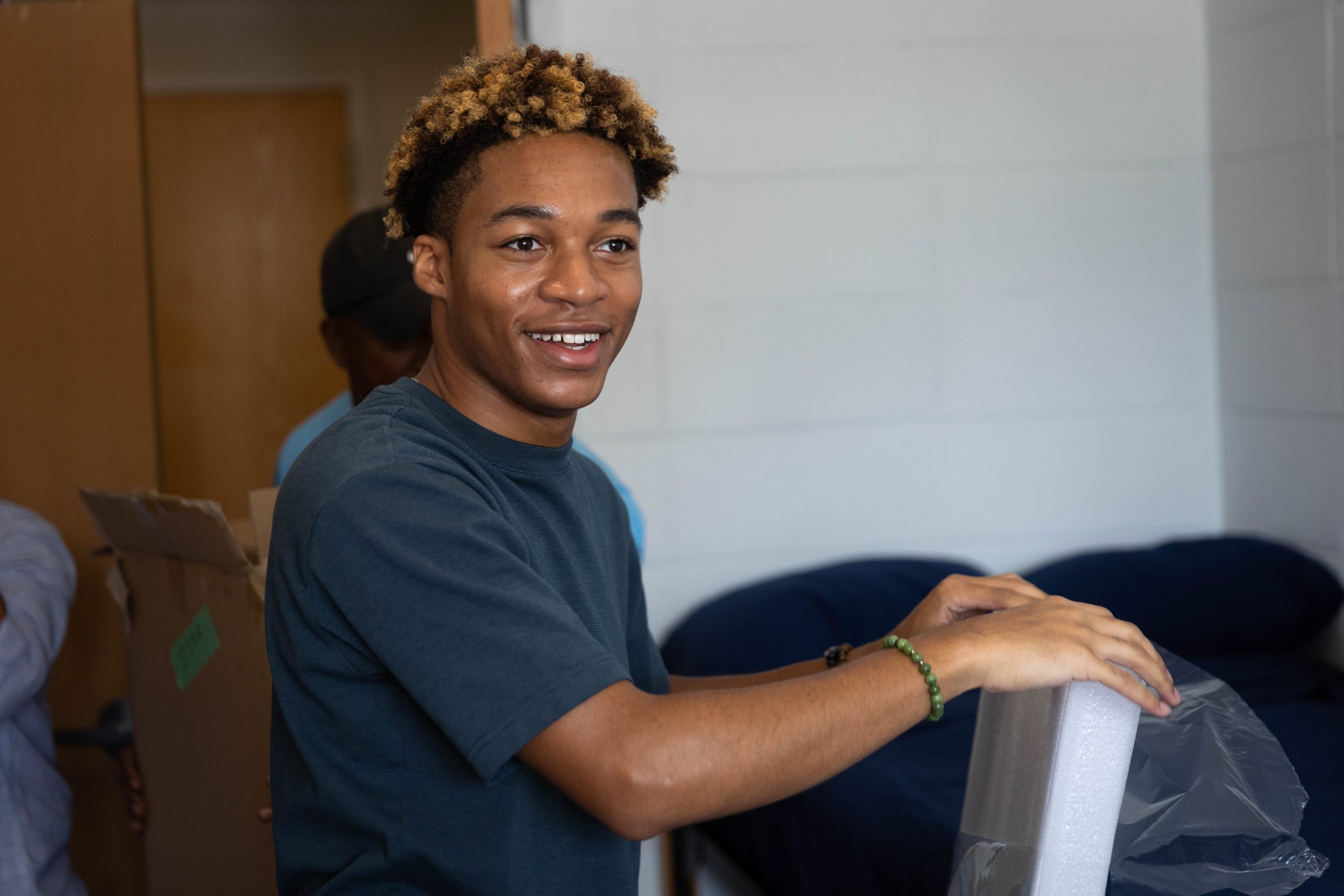 A male student smiles off-camera while unpacking in his dorm room during move-in.