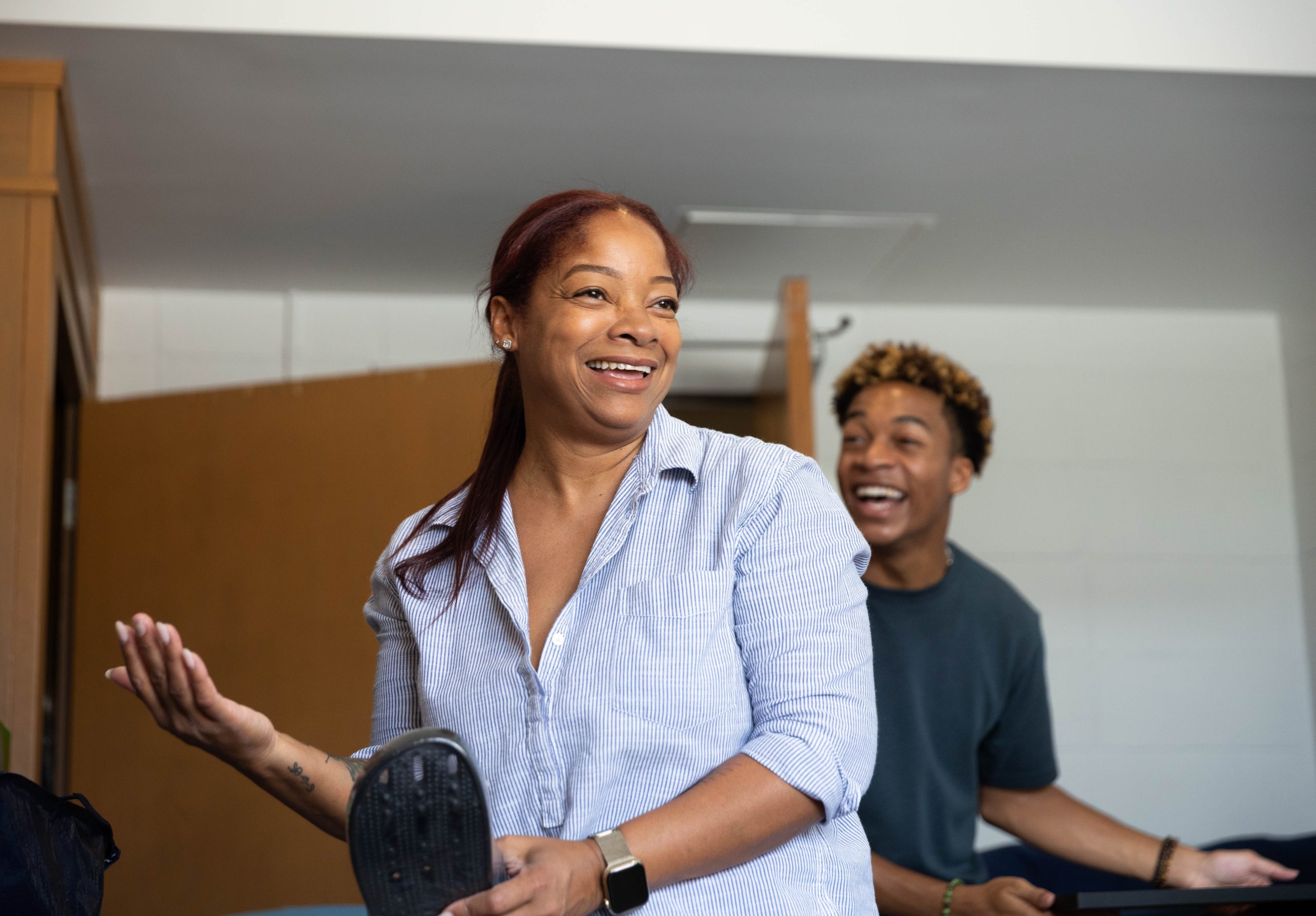 A mother holds up a flip flop and smiles as her son laughs in the background in his dorm room as they move in for the first time.