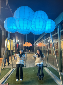 Two girls smile at each other while sitting on swings at a Georgetown Lights Display.