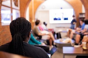 Back of a woman's head facing a room with people looking at a screen.