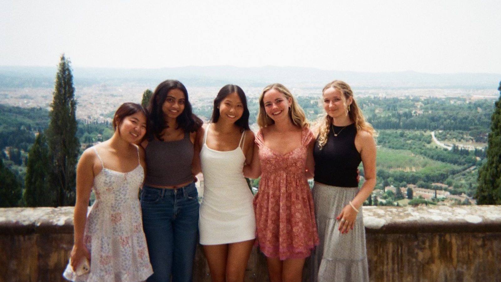Five girls stand smiling with the landscape of Italy behind them