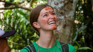 Woman with red face paint in a green shirt looking up in a rainforest