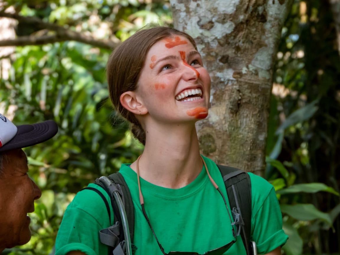 Woman with red face paint in a green shirt looking up in a rainforest