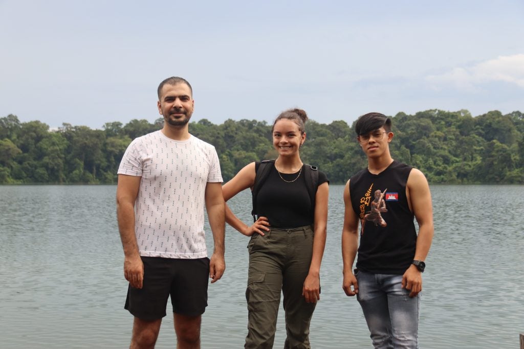 Kamiryn in between two men in front of a lake in Cambodia