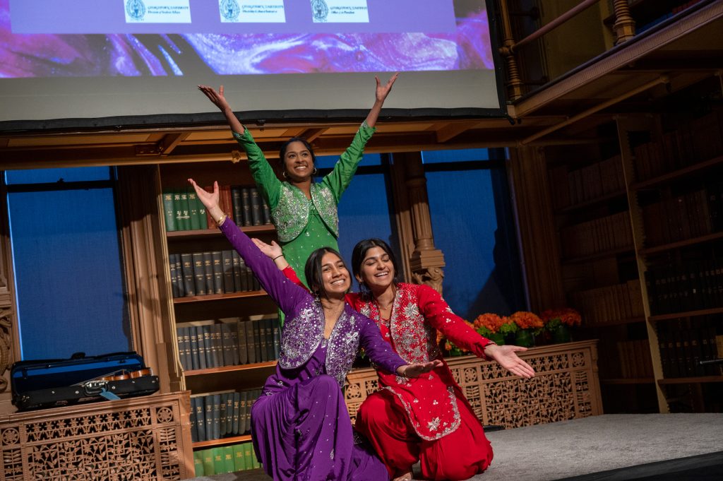 Three students dressed in bright red, purple and green outfits raise their arms up after performing a traditional Indian dance at a disability and the arts showcase at Georgetown. 