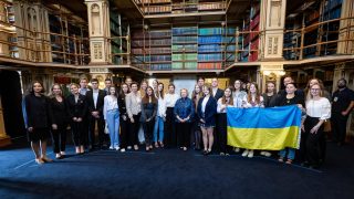 A group of Ukrainian students pose with the First Lady of Ukraine in a Georgetown library. One student holds up the yellow and blue Ukrainian flag.