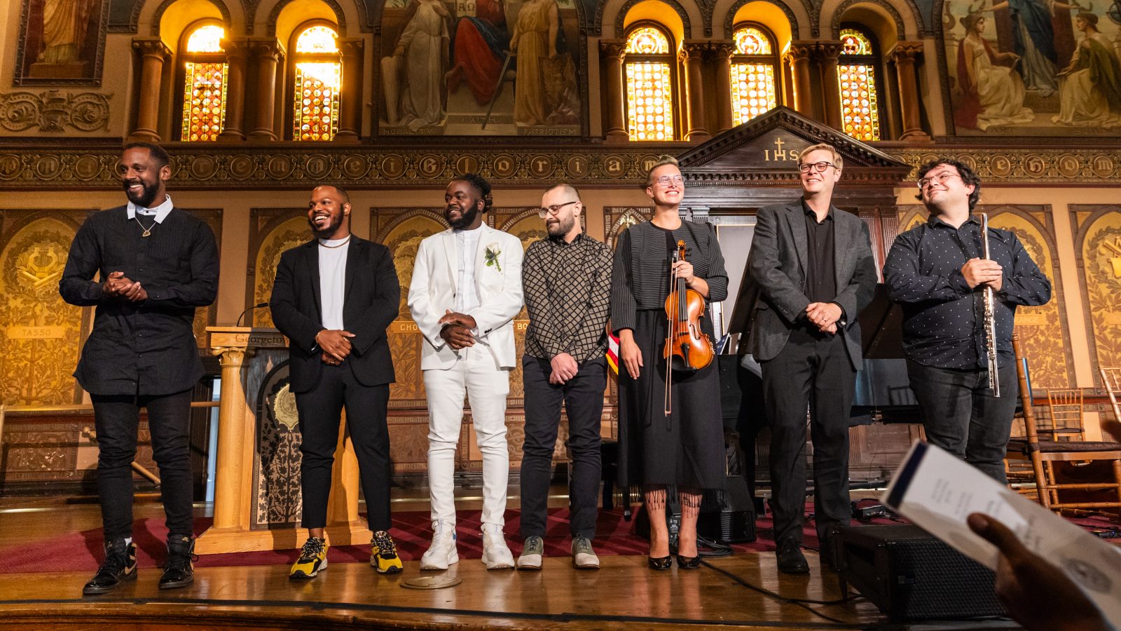 A group of musicians stand on stage of Georgetown&#039;s Gaston Hall after a live performance.