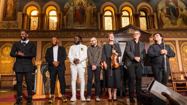 A group of musicians stand on stage of Georgetown&#039;s Gaston Hall after a live performance.