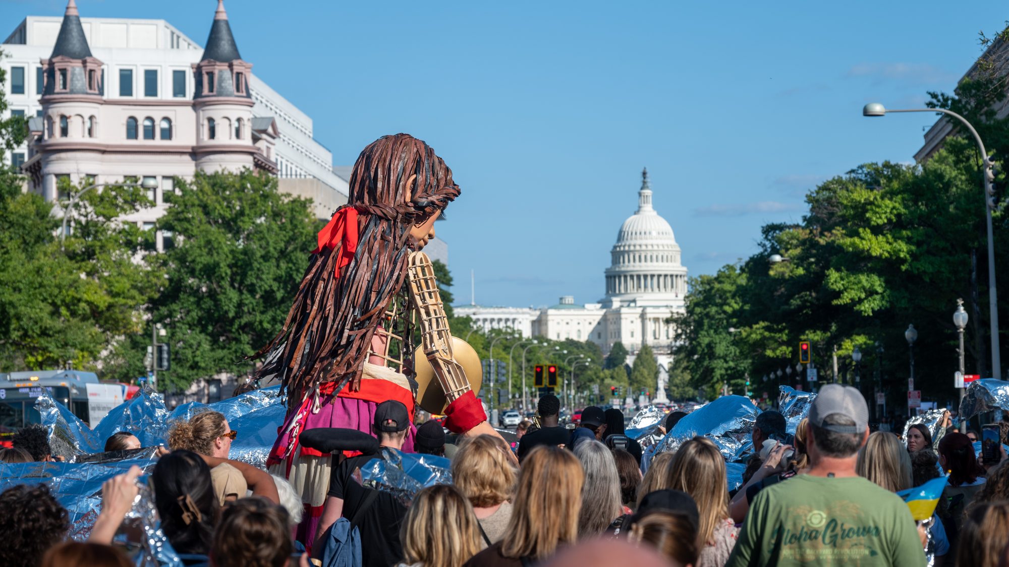 Little Amal, a puppet made to resemble a 10-year-old Syrian refugee, walks in a crowd toward the U.S. Capitol in the distance.