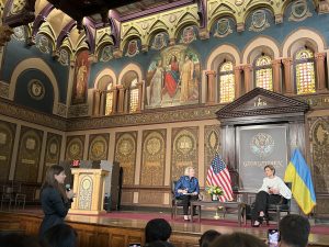 A Georgetown student from Ukraine stands before the First Lady of Ukraine in Georgetown's Gaston Hall and asks her a question. Behind the first lady is a blue and yellow Ukrainian flag.