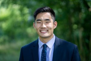 Zach Lee (C’25), a Georgetown student, wears a suit and tie and smiles at the camera.