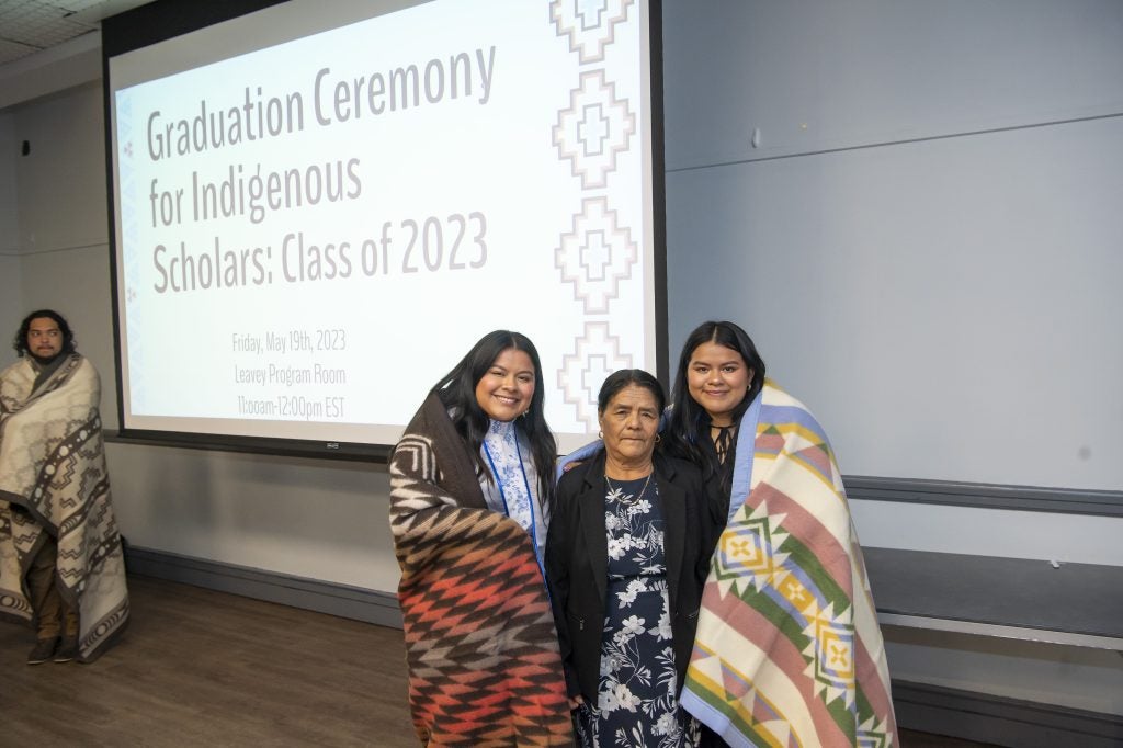 Two young women wrapped in traditional blankets standing with an older woman