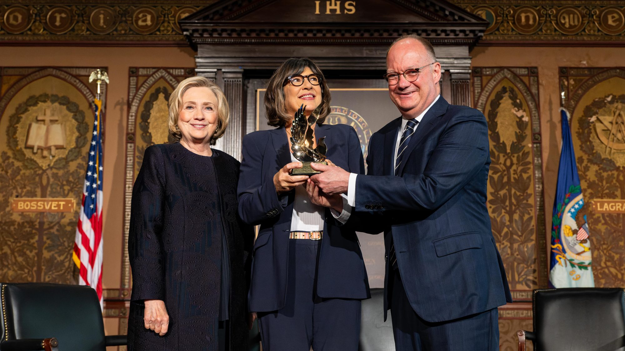 Hillary Clinton, Christiane Amanpour and Georgetown President John J. DeGioia stand on stage of Gaston Hall and Amanpour holds an award.