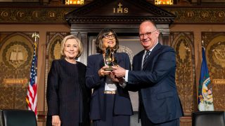 Hillary Clinton, Christiane Amanpour and Georgetown President John J. DeGioia stand on stage of Gaston Hall and Amanpour holds an award.