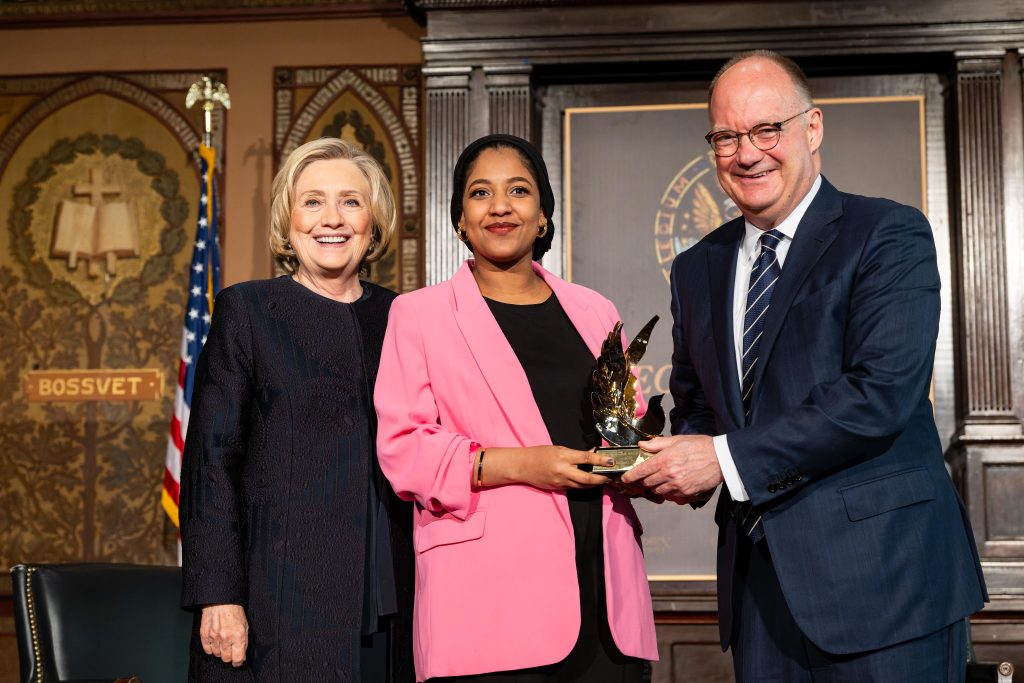 Hillary Clinton (left) and President John J. DeGioia (right) recognize Alaa Salah (center), a Sudanese democracy activist, civil society leader and human rights activist who wears a pink blazer and holds an award on the stage of Gaston Hall.