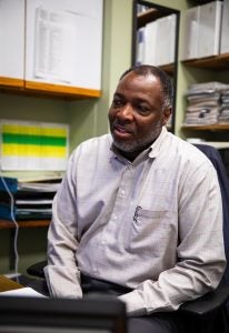 Al Brown sits in his office chair in front of white cabinets. He is wearing a white button-up shirt.