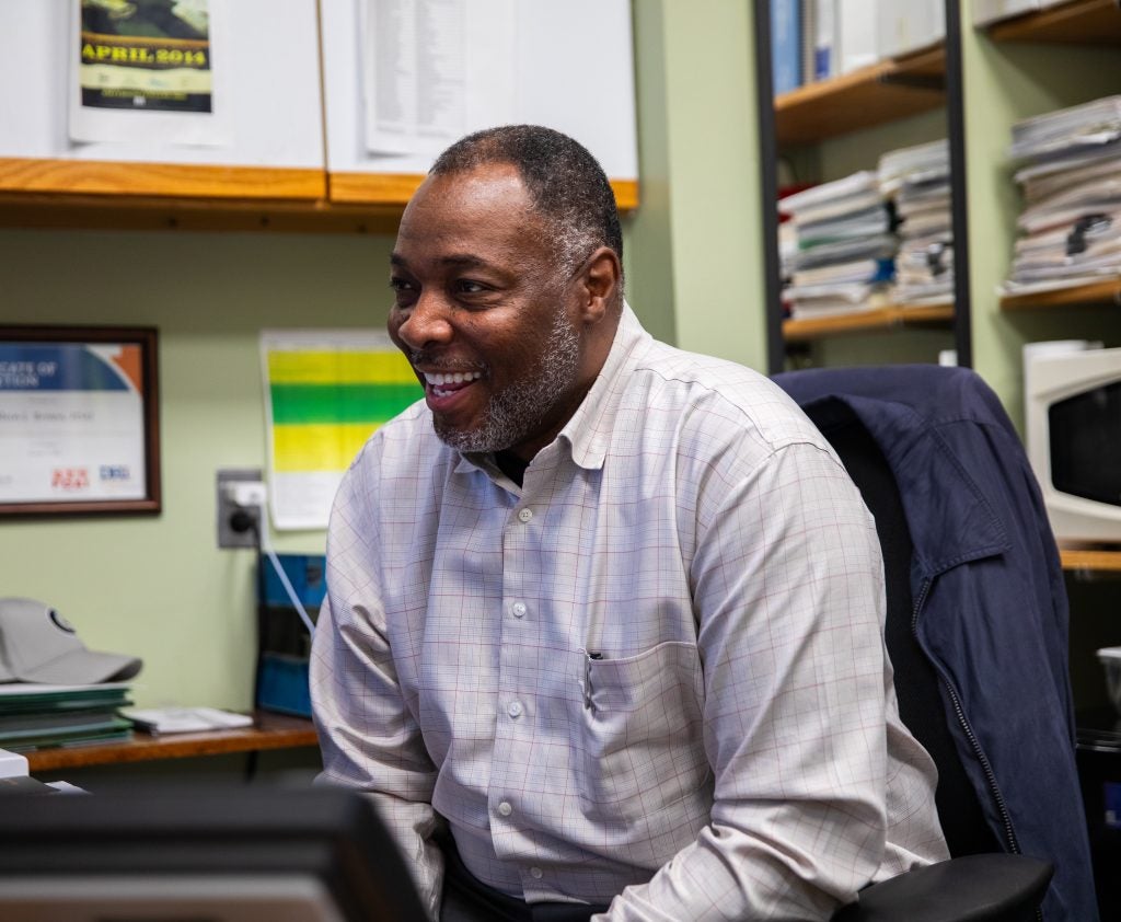 Al Brown laughs looking at his computer screen in his office, which is painted light green.