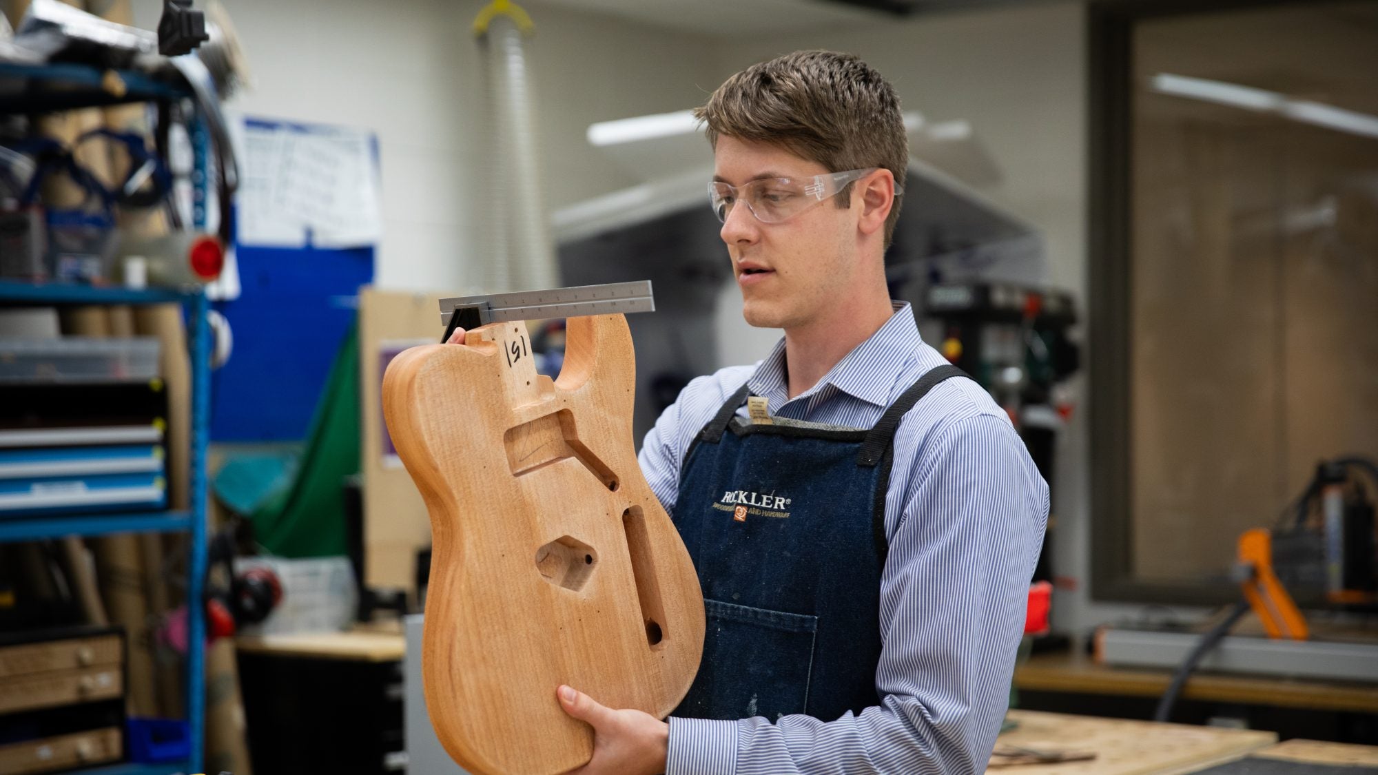 David Strout wears protective glasses and holds up the bottom of a wooden guitar in the Maker Hub on Georgetown&#039;s campus.