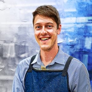 A graphical representation of David Strout wearing a blue apron over a blue collared shirt. He smiles at the camera.