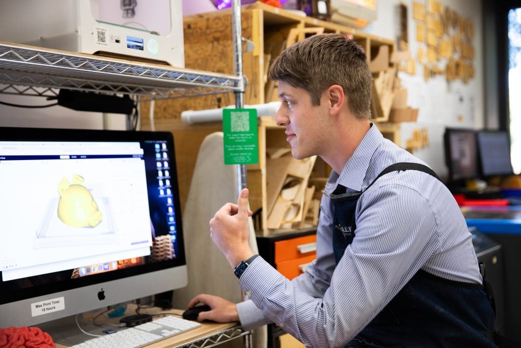 David Strout looks at a Mac computer while wearing an apron over a collared shirt.