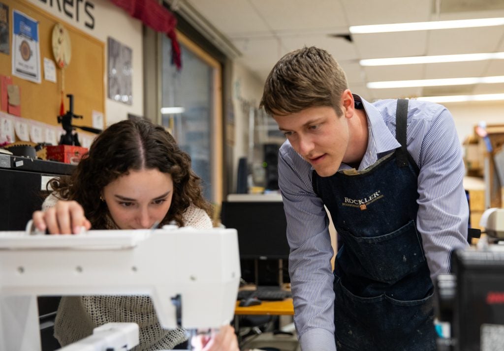 A staff member and student peer over a sewing machine in Georgetown's Maker Hub in the university library.