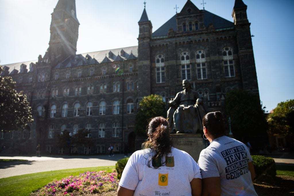 Two sisters stare up at John Carroll statue and the towers of Healy Hall on Georgetown's campus on a bright sunny day.