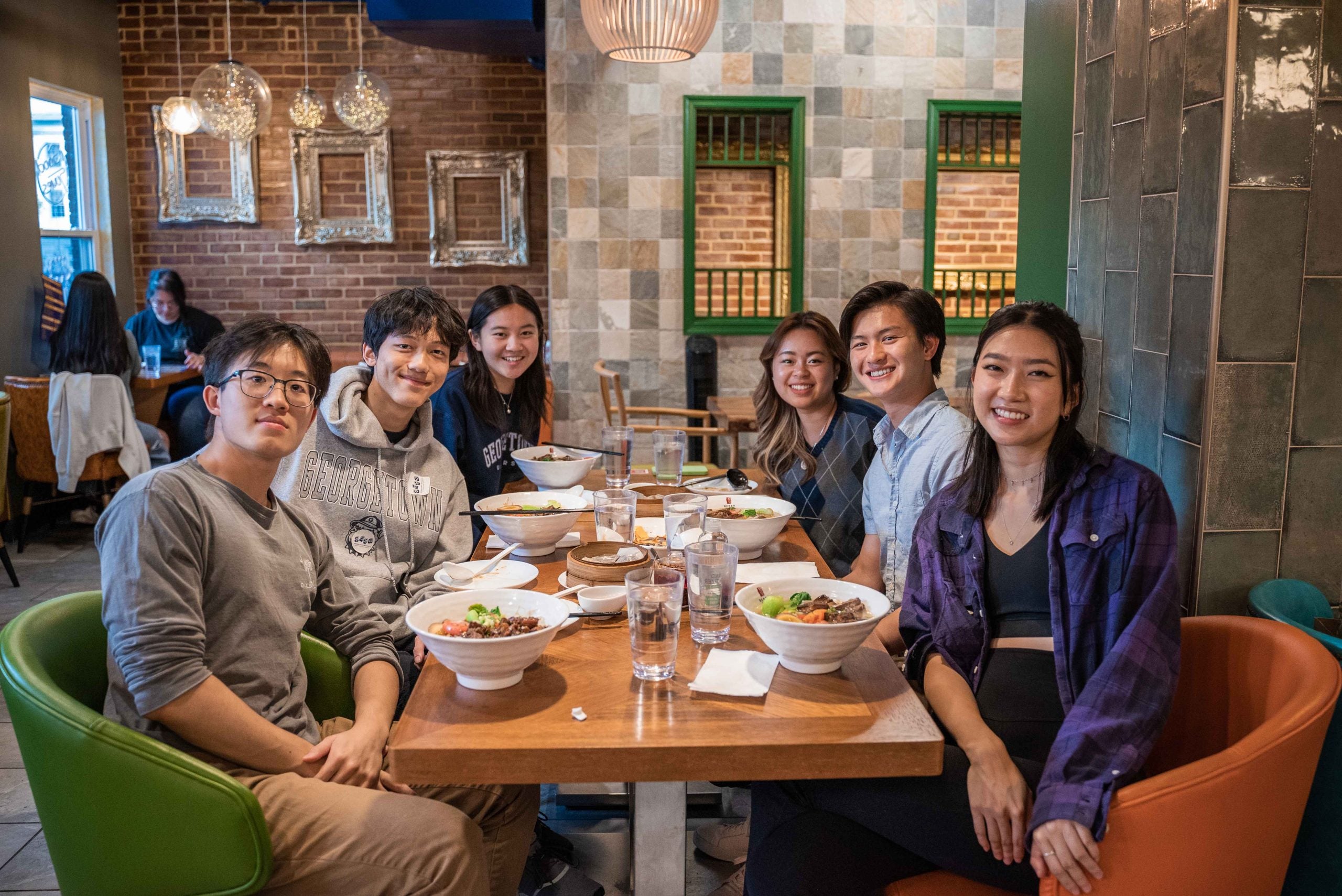 Six friends around a table for dinner, smiling at the camera