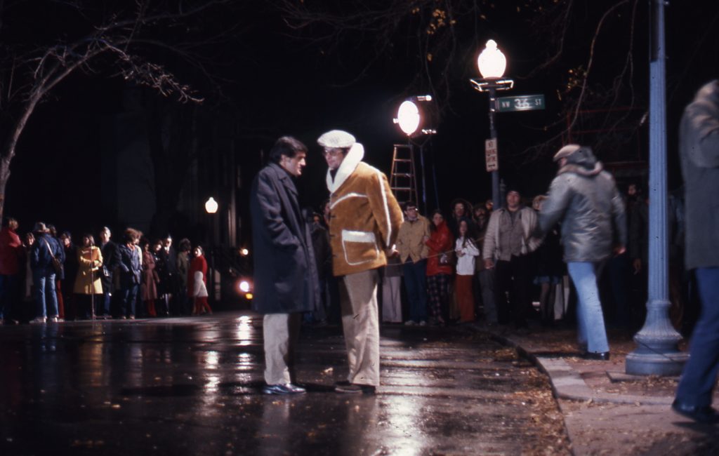 Two men talk together at night in the middle of a film set
