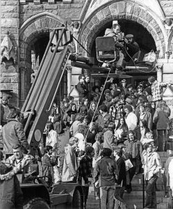 A film crew in front of the Healy Hall steps films a crowd of staged protestors