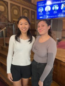 Two female students pose together in front of the stage in Gaston Hall after the 2023 Hillary Clinton Awards ceremony.