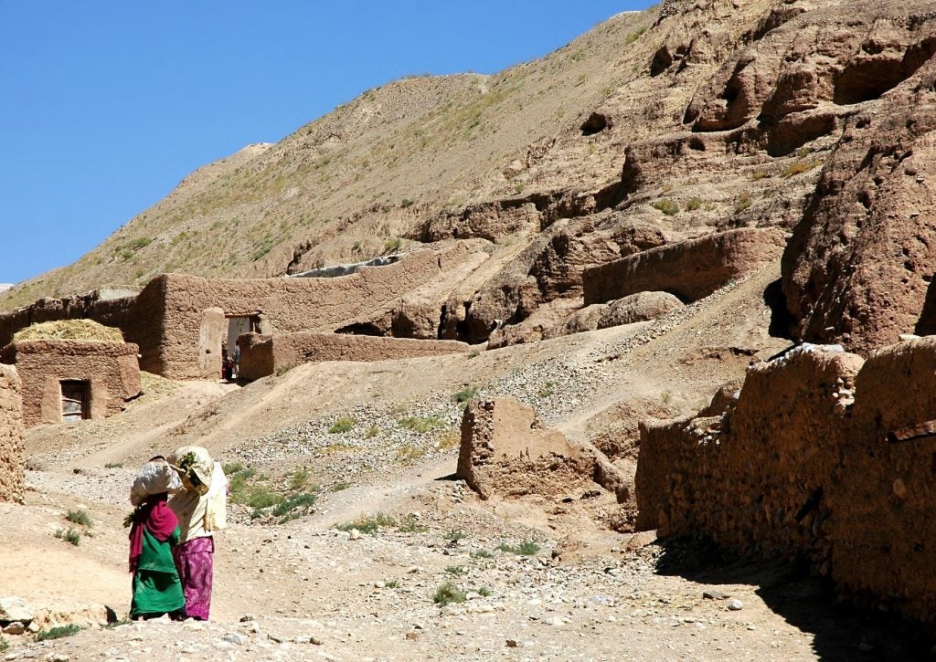 Two women carry goods on their heads as they walk home alongside a rocky mountain in Afghanistan.