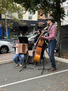 Three musicians perform in a parking lot off of Wisconsin Avenue. They have a violin, bass, and an accordion piano