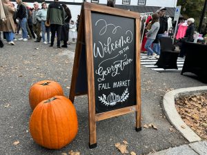 Pumpkins and chalkboard sign that reads "Welcome to the Georgetown Fall Market" in cursive