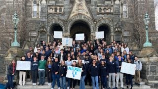 NAIMUN students stand on Healy steps for a group photo, holding NAIMUN signs