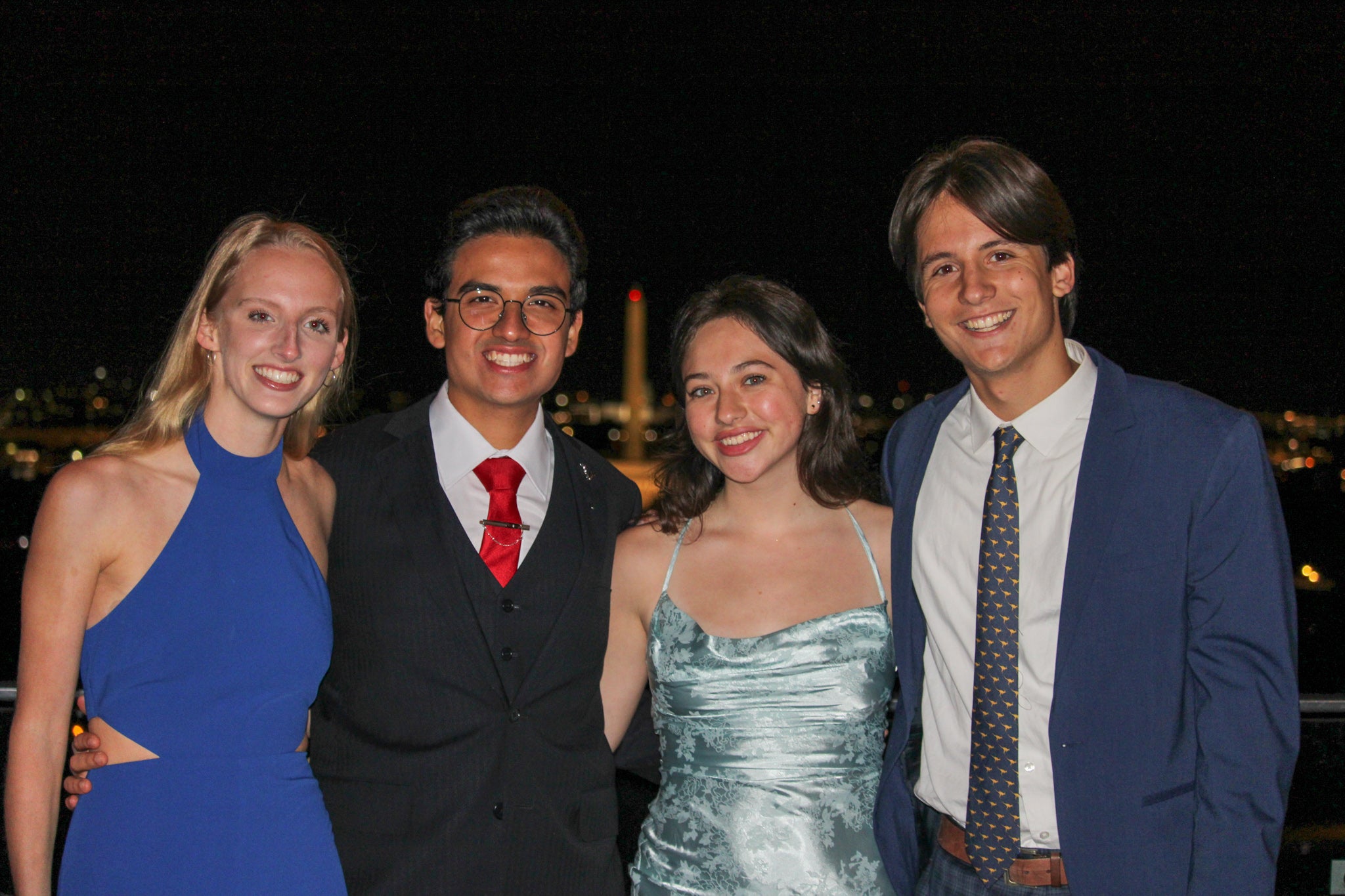 Four students in formal attire smile at the camera