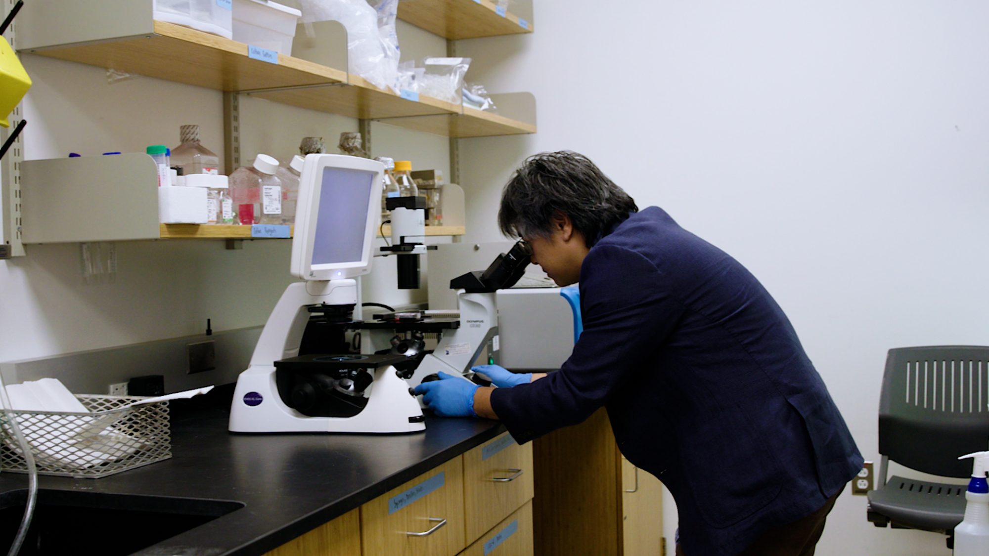 Jeffrey Huang looking into a microscope in a lab setting