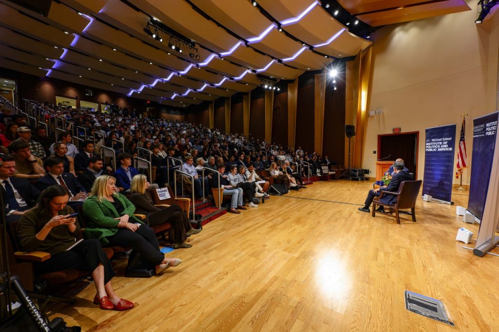 Two men on stage with a large crowd in Lohrfink Auditorium
