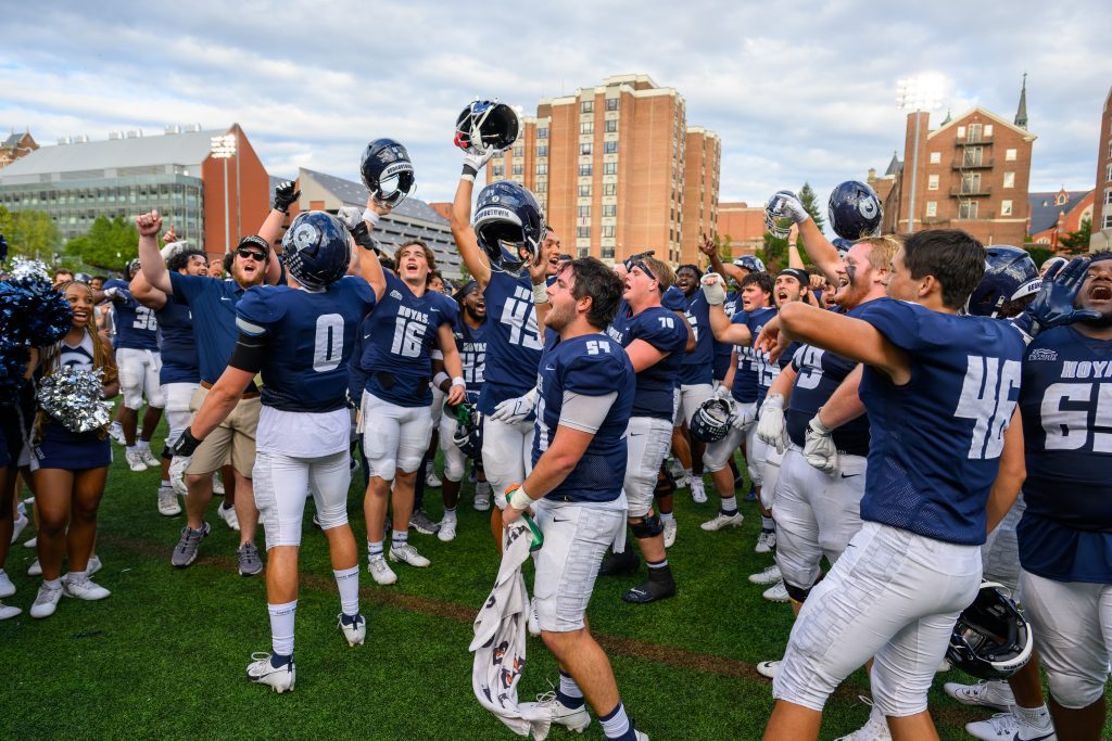 Georgetown's men's football team celebrates a win on the field by waving their blue helmets in the air.