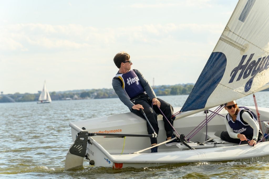 Two students sail a sailboat that leans on its right side toward the water in a race on the Chesapeake.