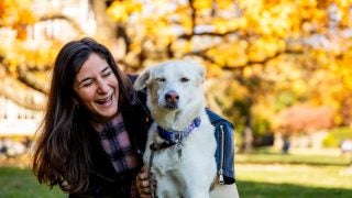 A woman kneeling with her white dog on a fall day