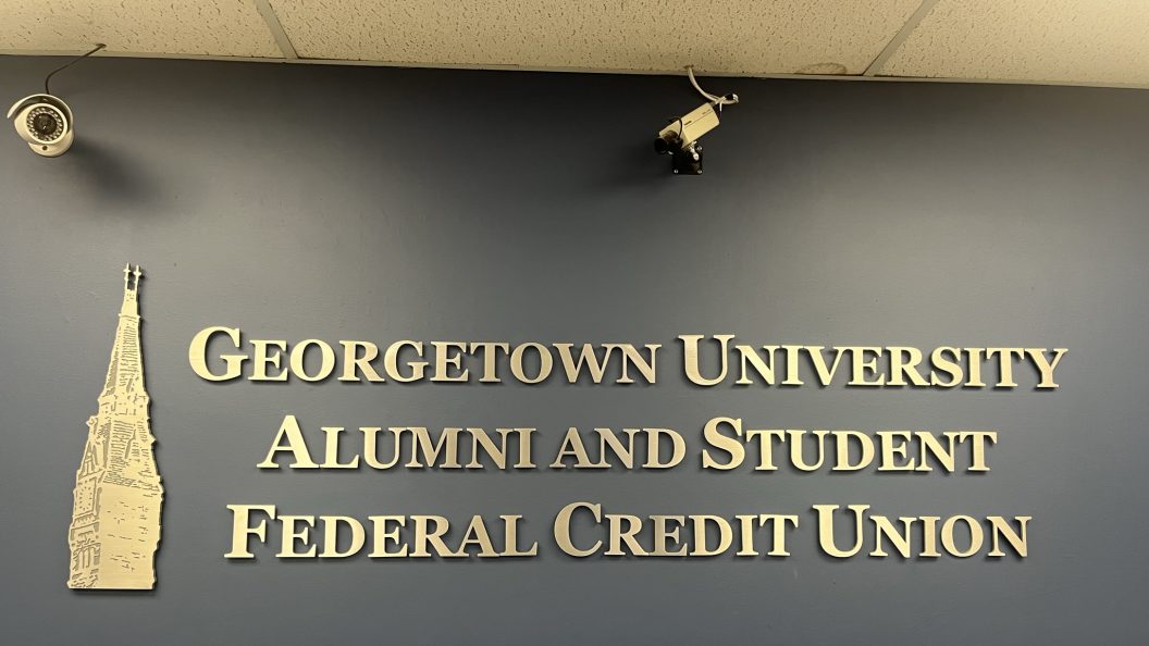 A wall with gold lettering introducing the Georgetown University Alumni and Student Federal Credit Union, with a gold Healy Tower next to it
